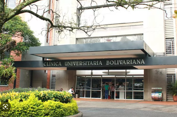 Pasillo moderno de la Clínica Universitaria Bolivariana con personal médico en bata blanca atendiendo a un paciente en camilla, en un entorno hospitalario de alta complejidad en Medellín, Colombia