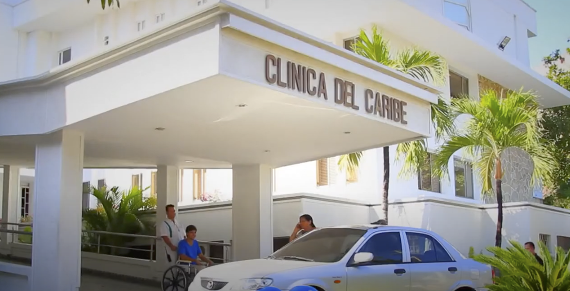 Médico especialista en bata blanca revisando los signos vitales de un paciente hospitalizado en una cama clínica de la Clínica del Caribe en Barranquilla, Colombia