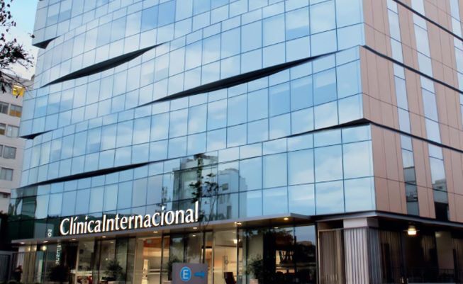 Médico especialista en bata blanca atendiendo a un paciente en una consulta presencial en la Clínica Internacional de Lima, con equipamiento médico moderno al fondo