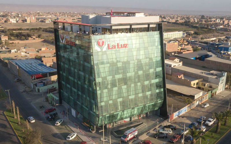 Fachada de la sede principal de Clínica La Luz en Av. Arequipa, Lima, con ingreso de pacientes y personal médico en el área de recepción