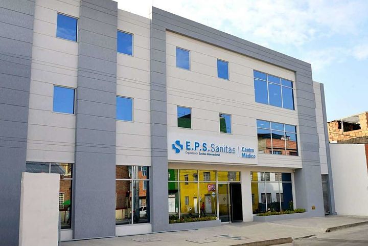 Fachada de una sede de EPS Sanitas en Colombia con personal administrativo atendiendo afiliados en mostrador de recepción