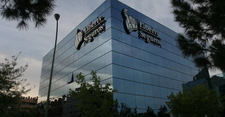 Ejecutivo de Liberty Seguros Colombia atendiendo a un cliente en una oficina corporativa con logo de la compañía visible al fondo