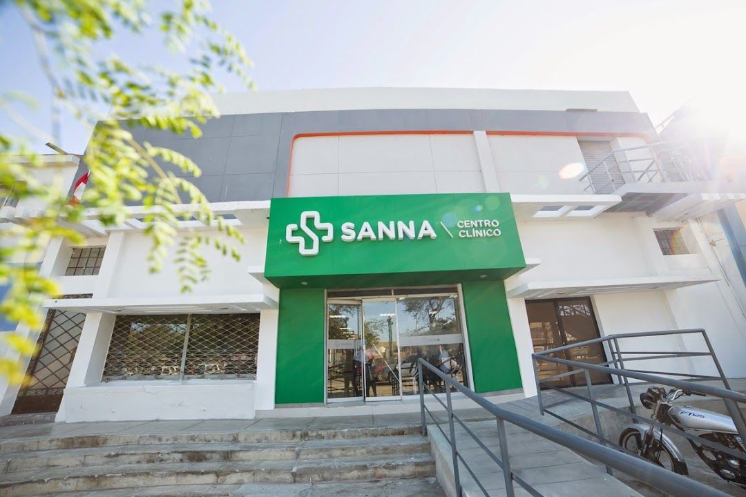 Médico atendiendo a un paciente en consultorio del Centro Clínico Talara de la red SANNA en Piura, con equipamiento clínico moderno al fondo